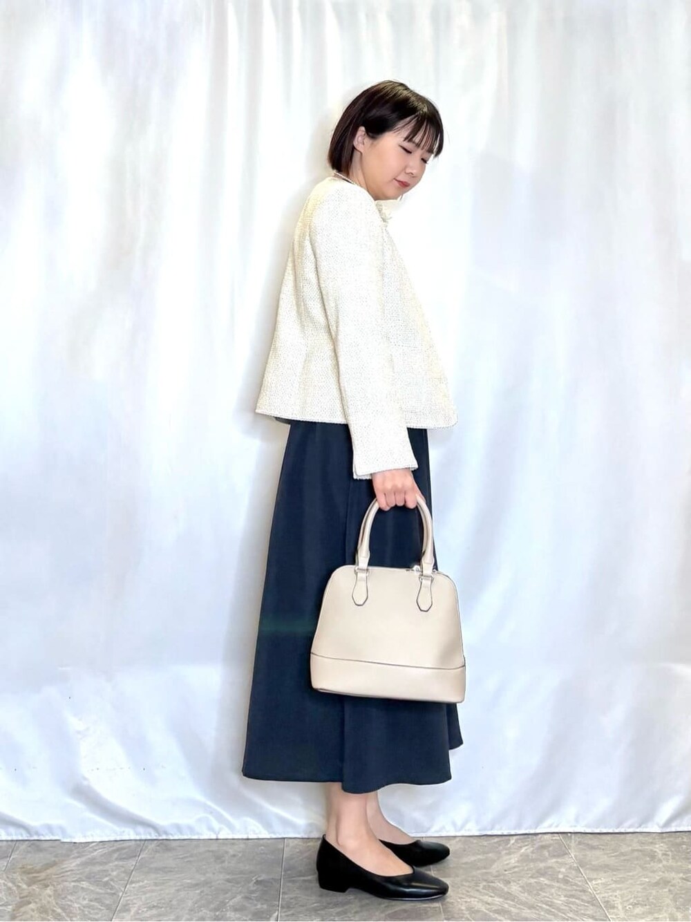 ホワイト系のノーカラージャケット、グレー系のトートバッグ、ブラック系のパンプスを着用したレディースの春コーディネートの2枚目の写真