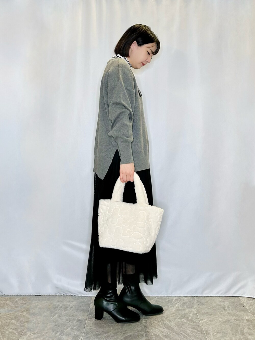 ベージュ系のトートバッグ、ブラック系のブーツ、グレー系のニット/セーターを着用したレディースの秋コーディネートの2枚目の写真