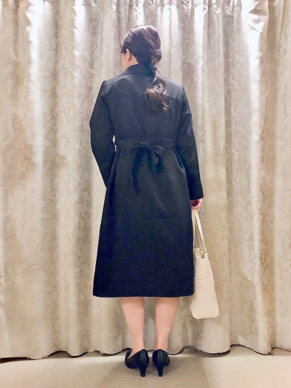 ホワイト系のトートバッグ、ブラック系のパンプス、ブラック系のトレンチコートを着用したレディースの春コーディネートの3枚目の写真