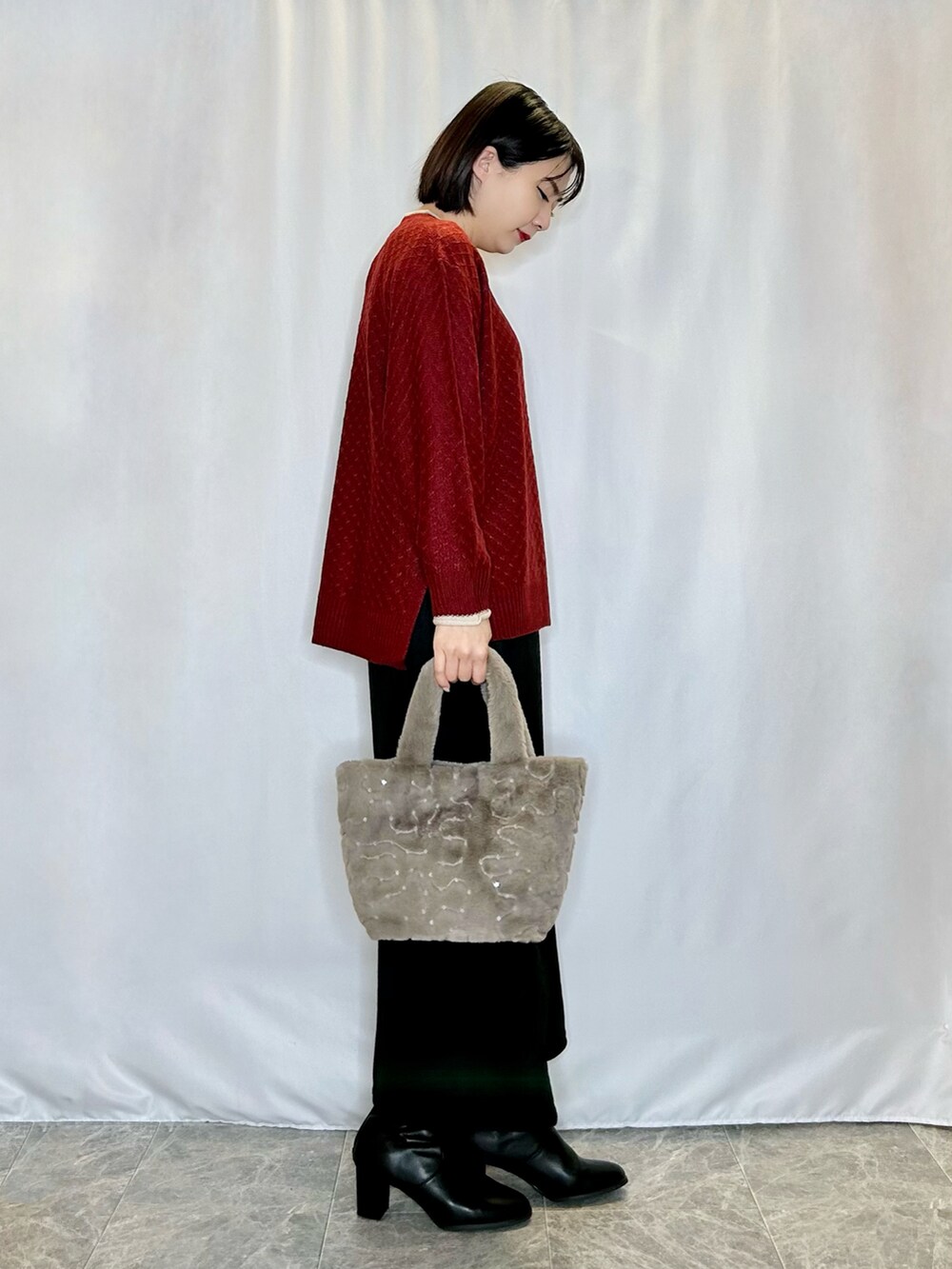 レッド系のニット/セーター、ベージュ系のトートバッグ、ブラック系のスカートを着用したレディースの冬コーディネートの2枚目の写真