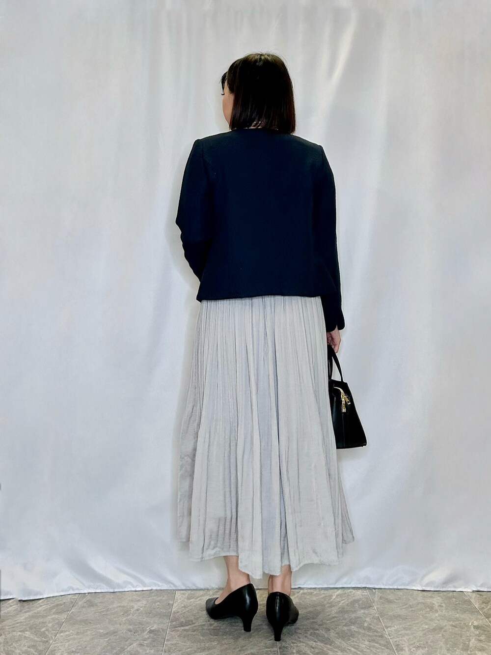 グレー系のスカート、ブラック系のパンプス、ブラック系のトートバッグを着用したレディースの冬コーディネートの3枚目の写真