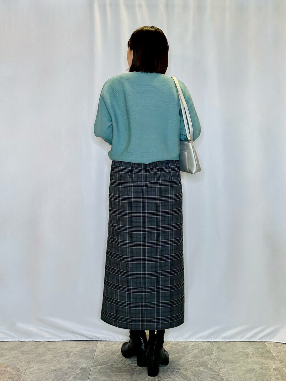 ブラック系のブーツ、シルバー系のショルダーバッグ、ブラック系のスカートを着用したレディースの秋コーディネートの3枚目の写真