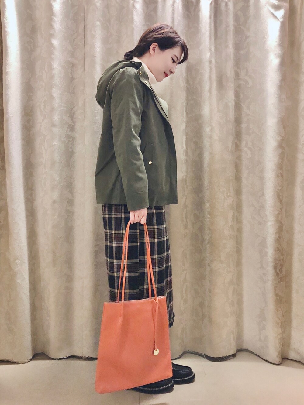 オレンジ系のトートバッグ、ブラック系のドレスシューズ、グリーン系のブルゾンを着用したレディースの秋コーディネートの2枚目の写真