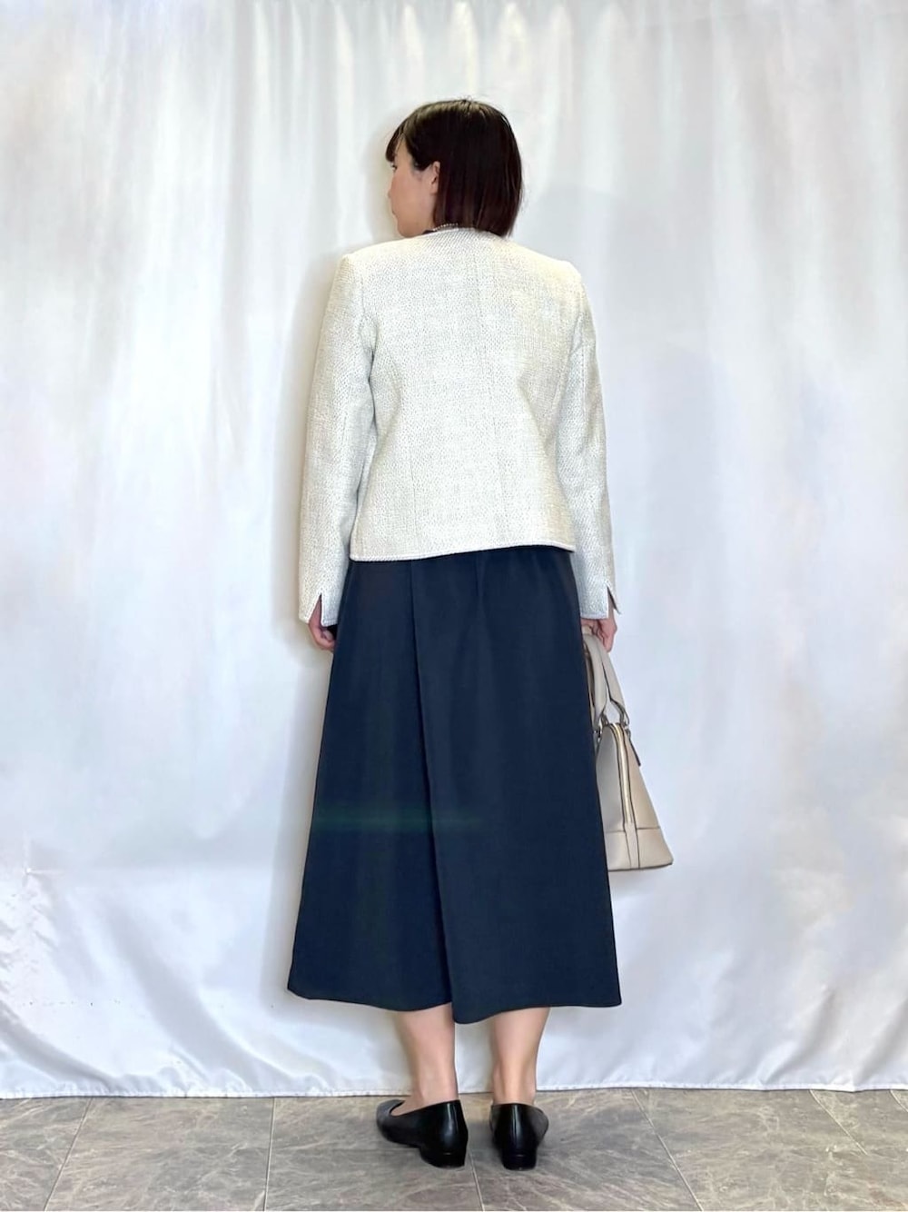 ホワイト系のノーカラージャケット、グレー系のトートバッグ、ブラック系のパンプスを着用したレディースの春コーディネートの3枚目の写真
