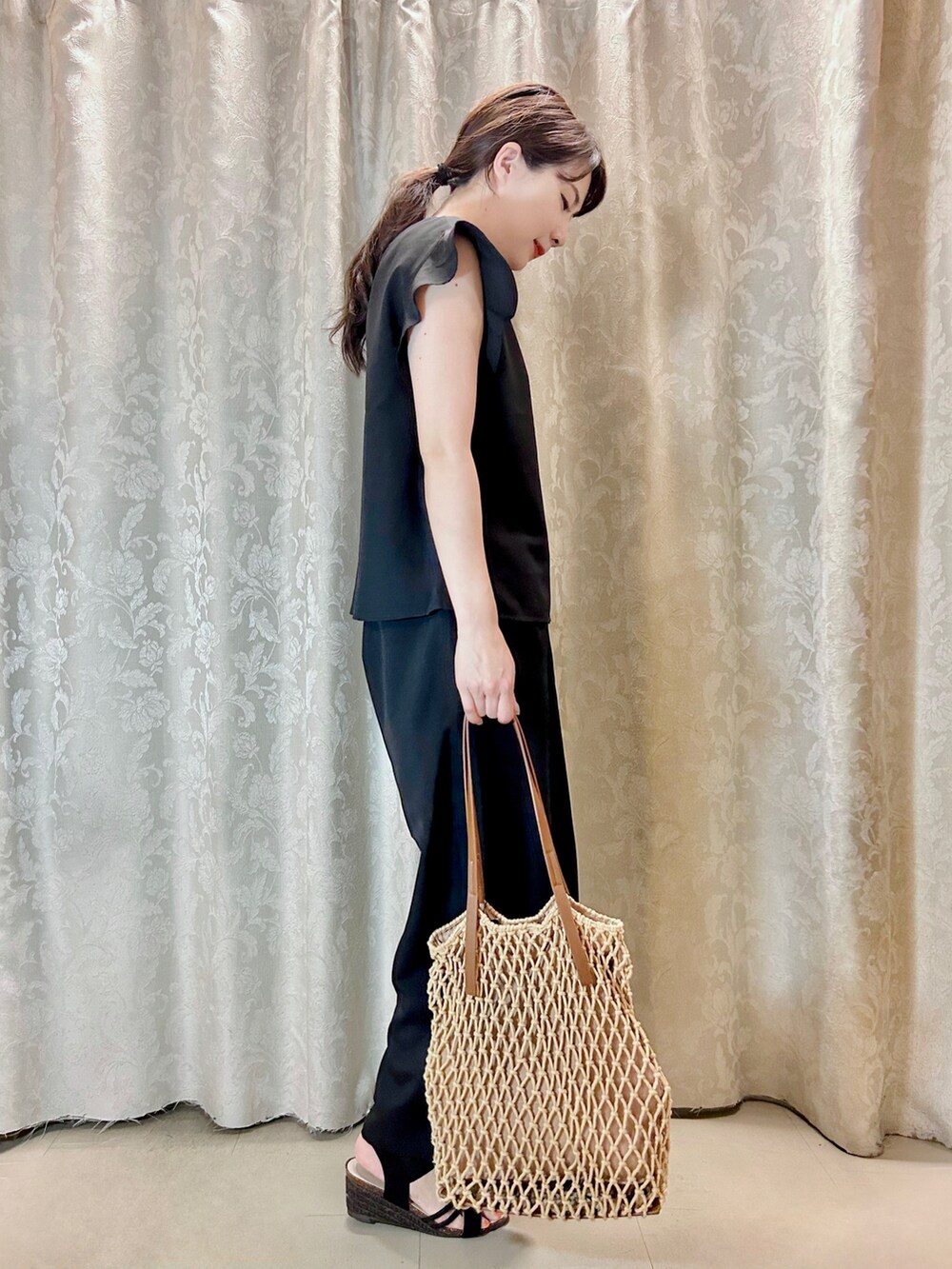 ブラウン系のトートバッグ、ブラック系のサンダル、ブラック系のシャツ/ブラウスを着用したレディースの夏コーディネートの2枚目の写真