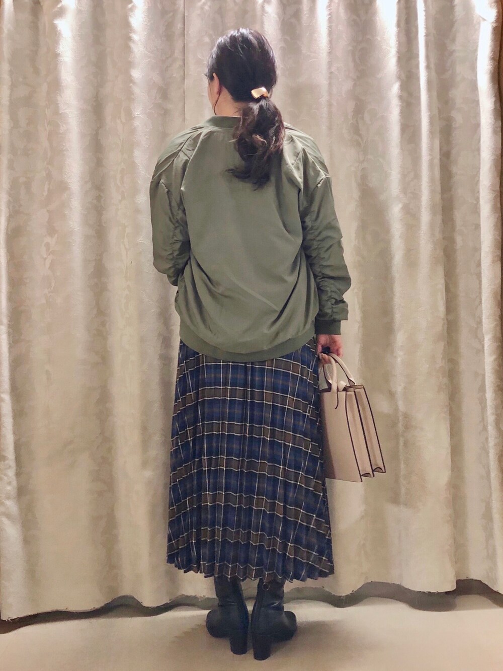 グリーン系のブルゾン、ブルー系のスカート、ブラック系のブーツを着用したレディースの秋コーディネートの3枚目の写真