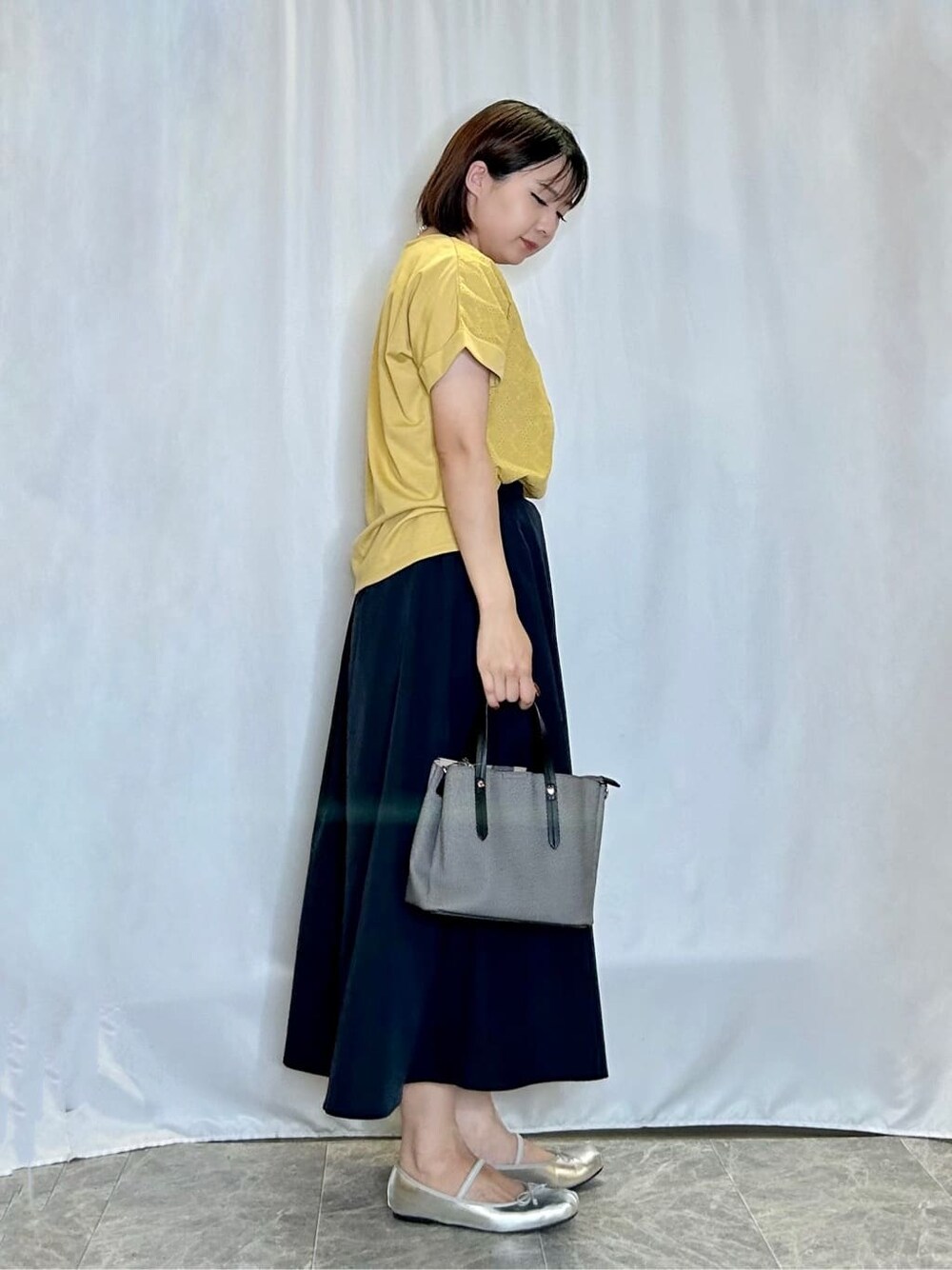 イエロー系のTシャツ/カットソー、ブルー系のスカート、ブラック系のトートバッグを着用したレディースの夏コーディネートの2枚目の写真