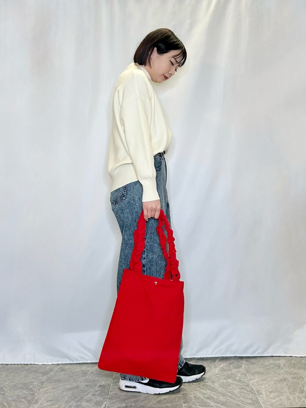 ブルー系のその他パンツ、レッド系のトートバッグ、ホワイト系のニット/セーターを着用したレディースの冬コーディネートの2枚目の写真