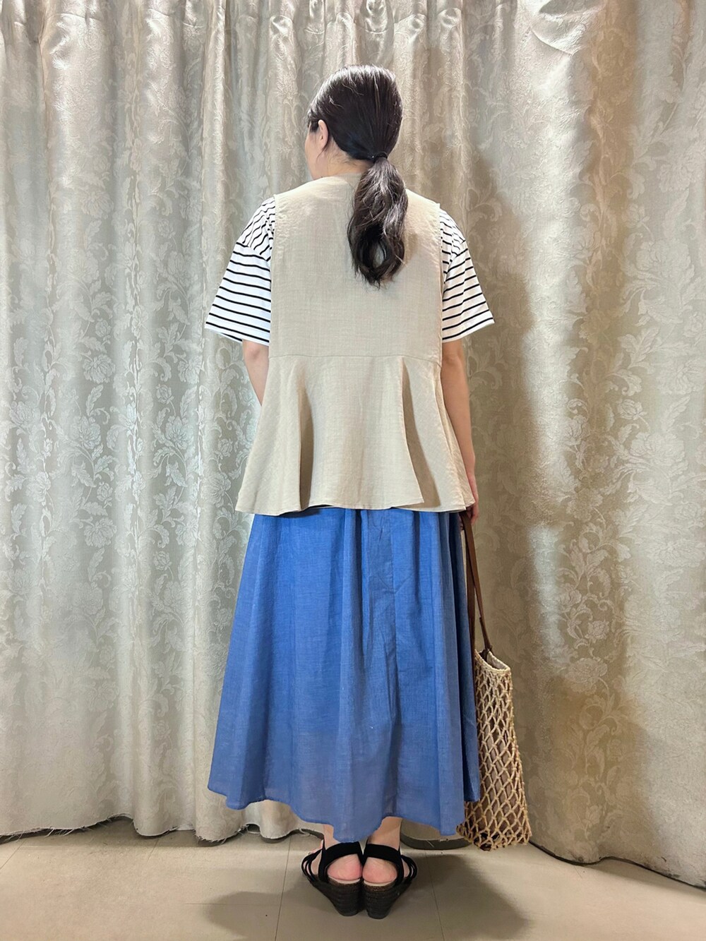 ブラウン系のトートバッグ、ブラック系のサンダル、ブルー系のスカートを着用したレディースの春コーディネートの3枚目の写真