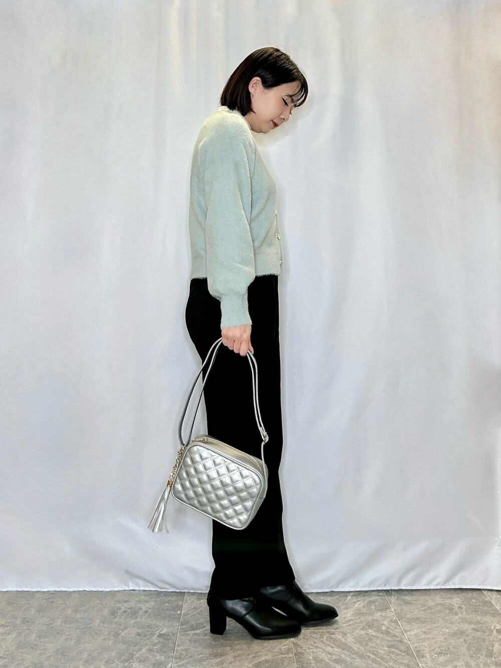 シルバー系のショルダーバッグ、ブラック系のブーツ、グリーン系のカーディガン/ボレロを着用したレディースの冬コーディネートの2枚目の写真