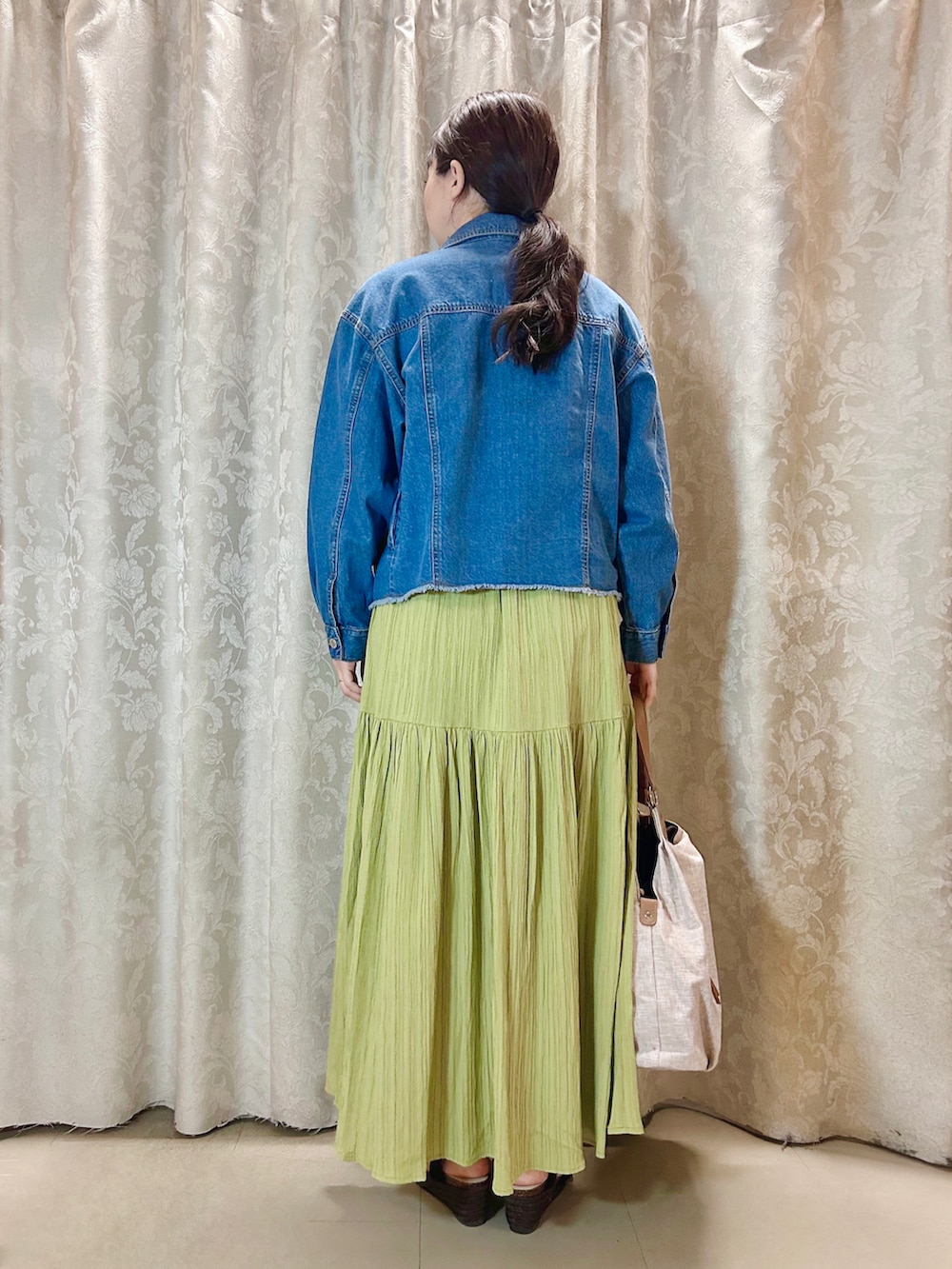 ベージュ系のトートバッグ、グリーン系のスカート、ブルー系のデニムジャケットを着用したレディースの春コーディネートの3枚目の写真