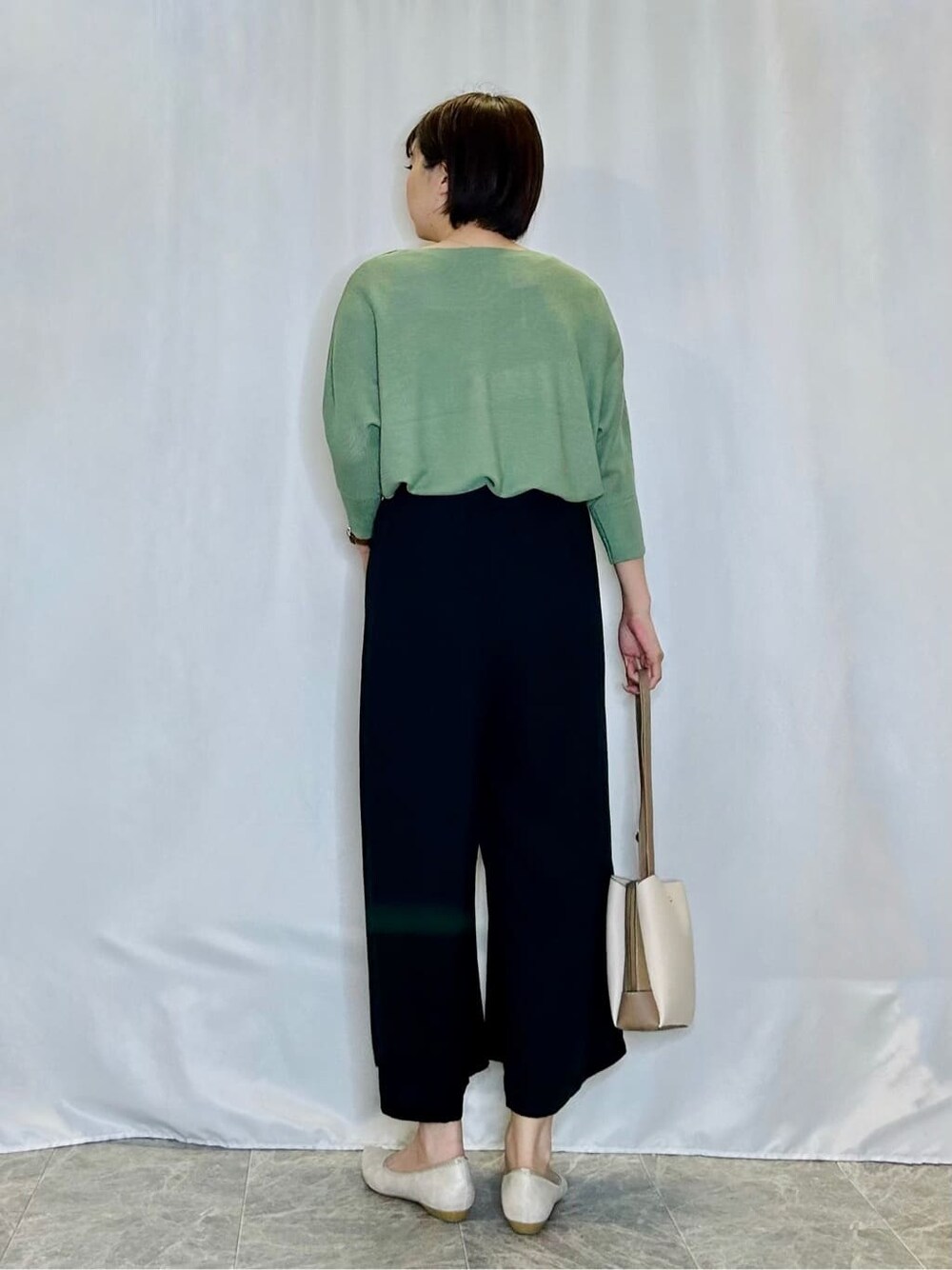 グリーン系のニット/セーター、ブルー系のその他パンツ、ゴールド系のその他シューズを着用したレディースの春コーディネートの3枚目の写真