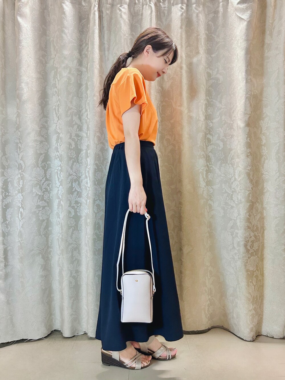 ホワイト系のショルダーバッグ、オレンジ系のTシャツ/カットソー、ゴールド系のサンダルを着用したレディースの夏コーディネートの2枚目の写真