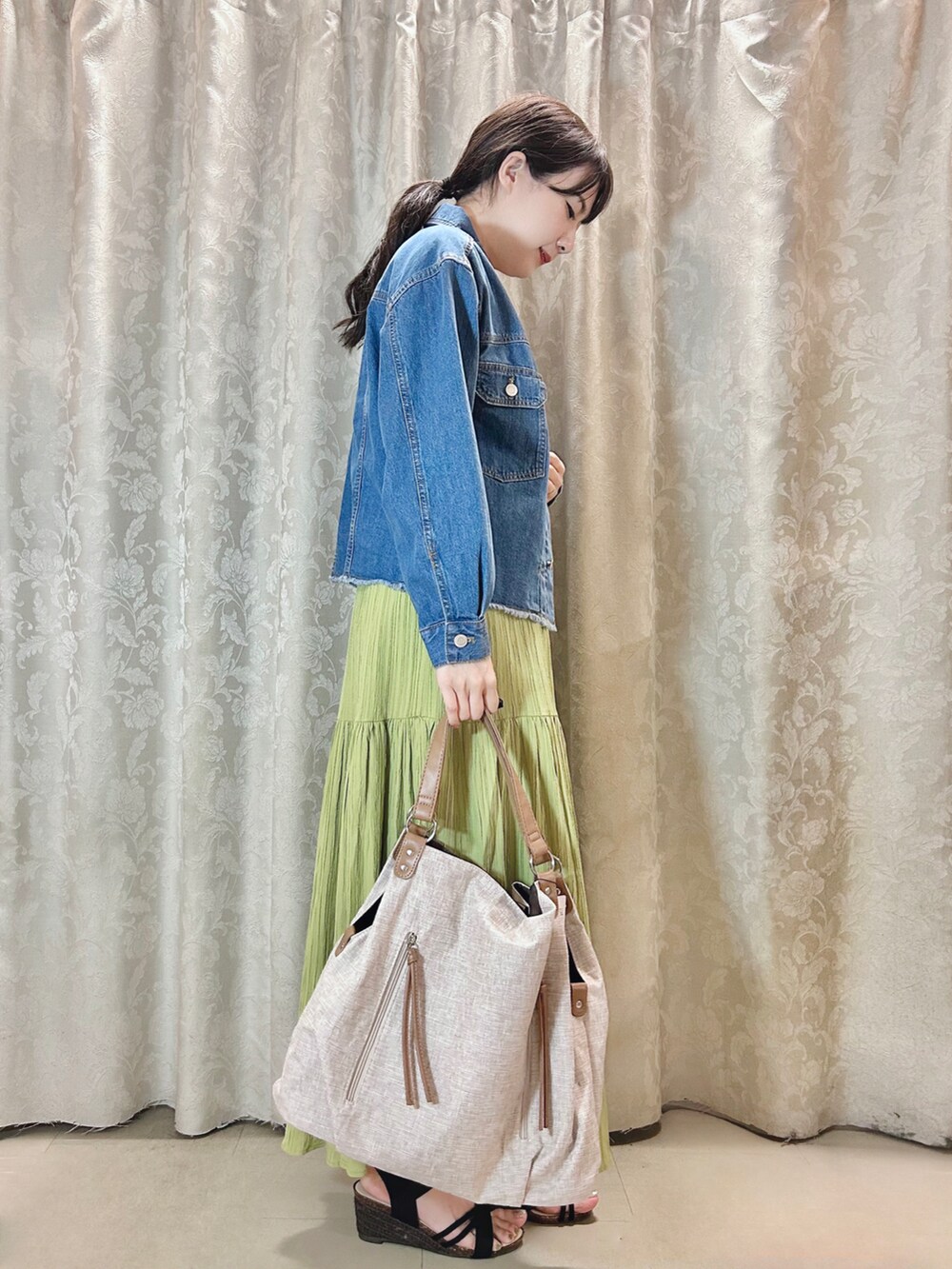 ベージュ系のトートバッグ、グリーン系のスカート、ブルー系のデニムジャケットを着用したレディースの春コーディネートの2枚目の写真