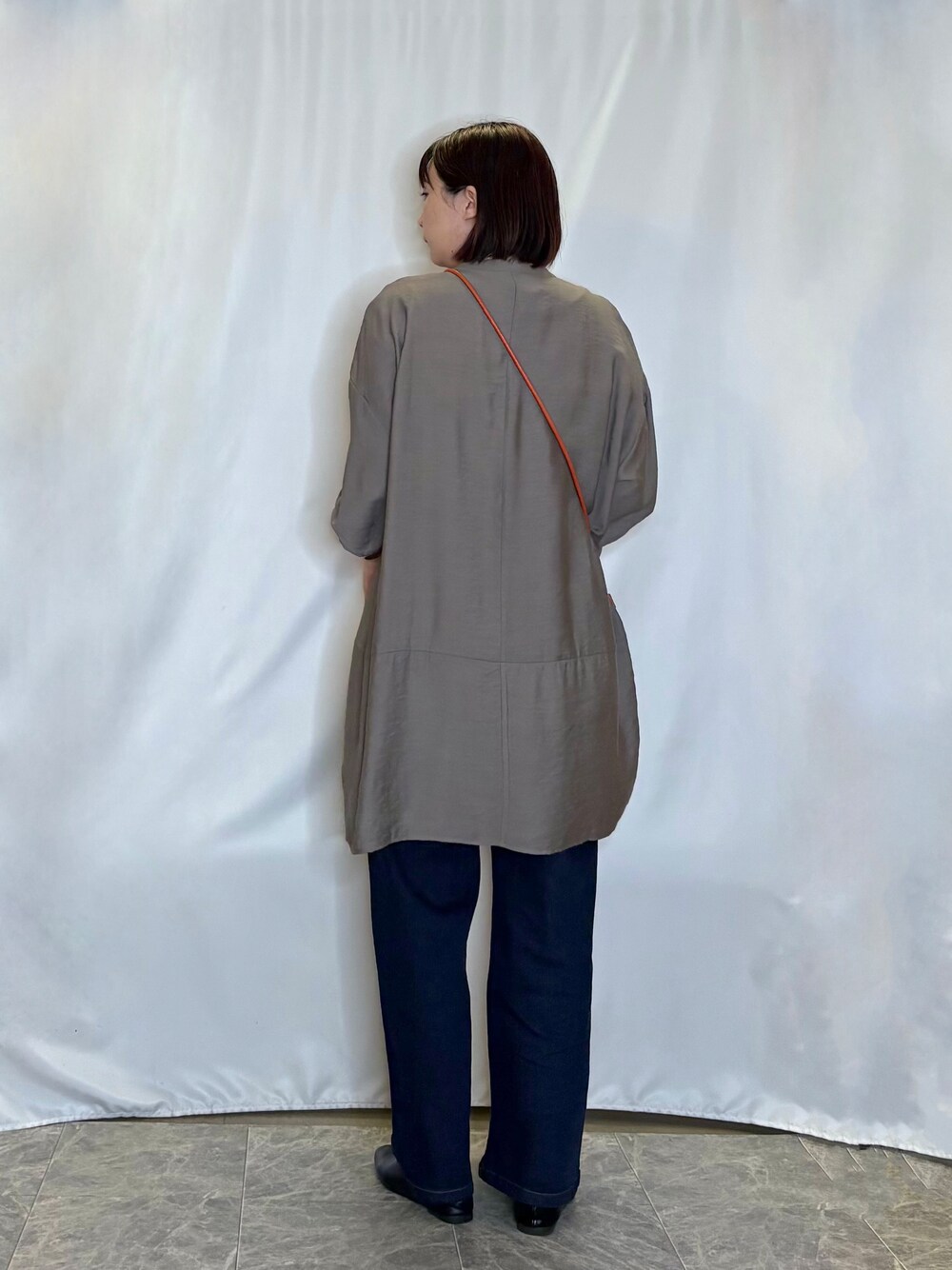 ブラウン系のワンピース、ブルー系のデニムパンツ、オレンジ系のショルダーバッグを着用したレディースの秋コーディネートの3枚目の写真