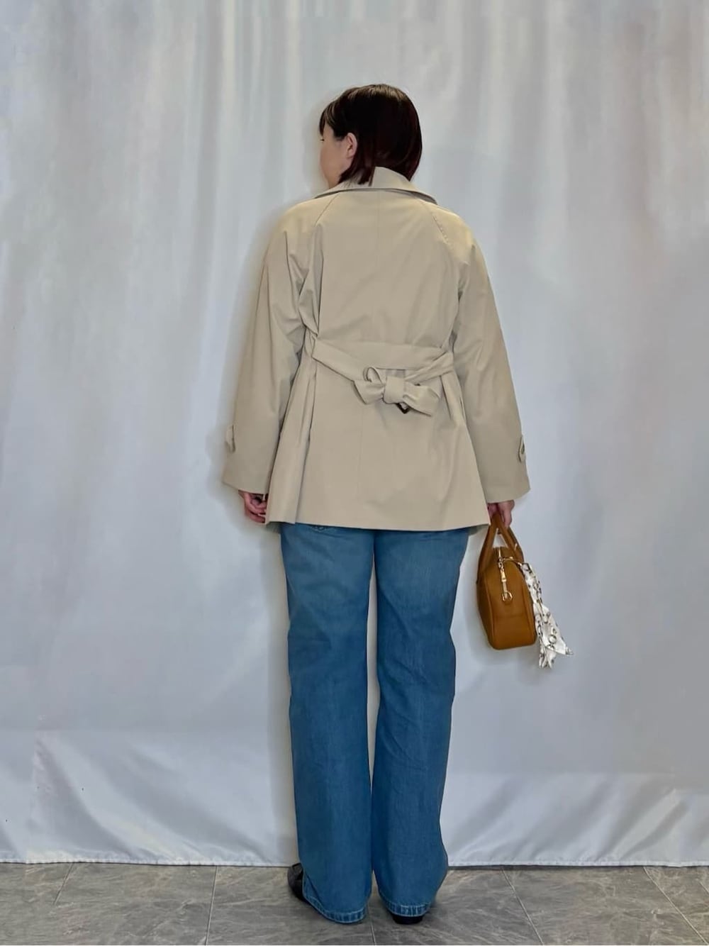 ベージュ系のトレンチコート、レッド系のニット/セーター、ブルー系のデニムパンツを着用したレディースの冬コーディネートの3枚目の写真