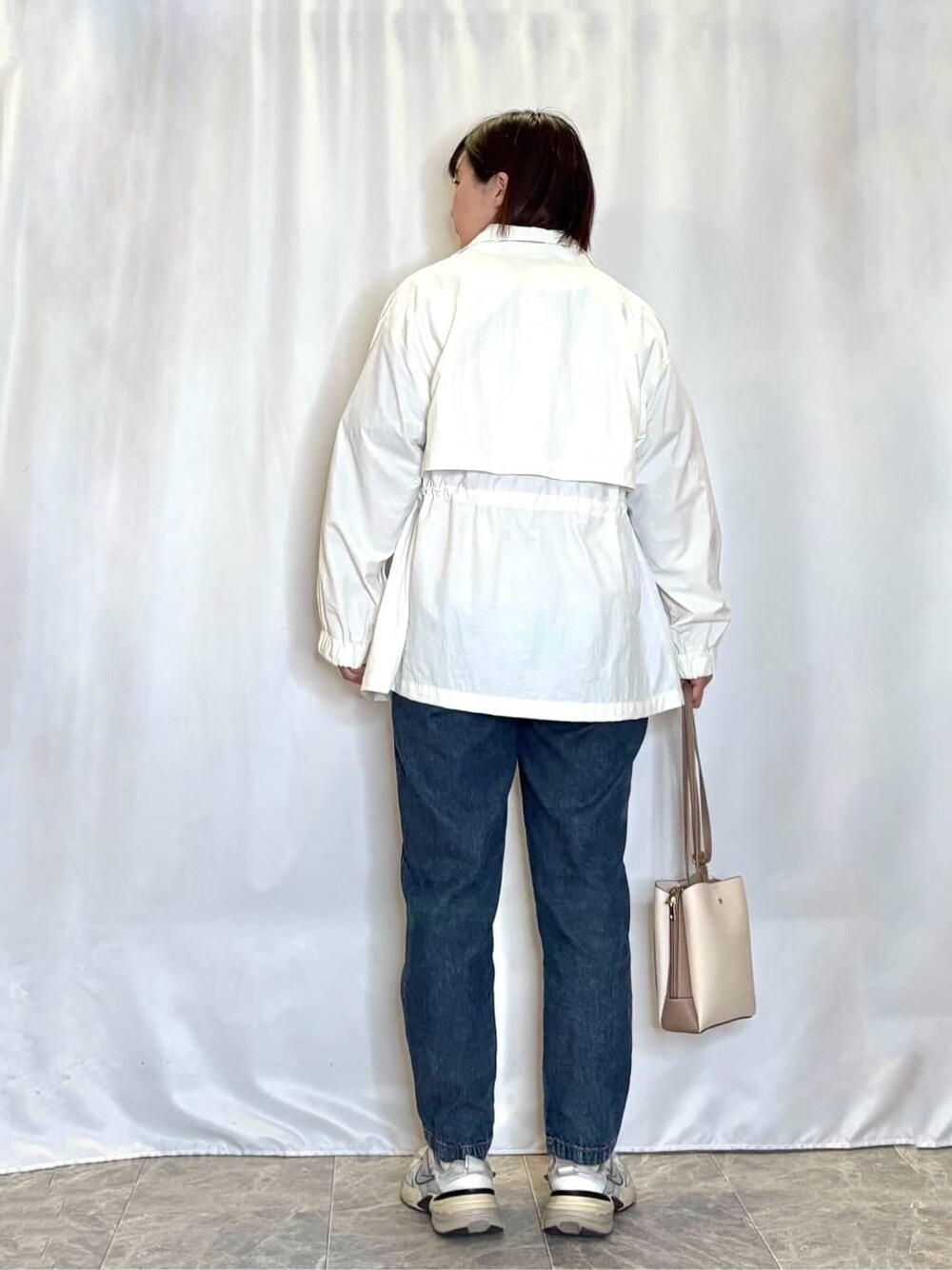 ホワイト系のブルゾン、オレンジ系のニット/セーター、ブルー系のデニムパンツを着用したレディースの春コーディネートの3枚目の写真
