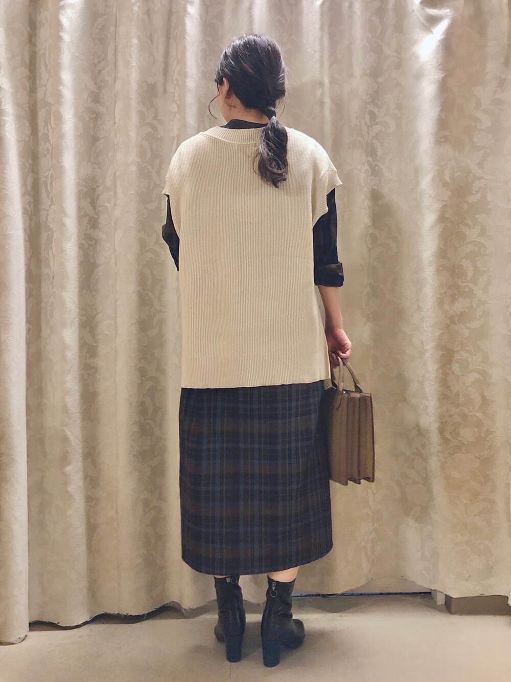 ベージュ系のショルダーバッグ、ブラック系のブーツ、ベージュ系のベストを着用したレディースの秋コーディネートの3枚目の写真