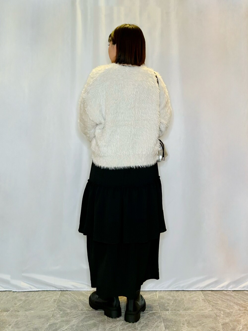 ブラック系のスカート、シルバー系のショルダーバッグ、ブラック系のブーツを着用したレディースの秋コーディネートの3枚目の写真