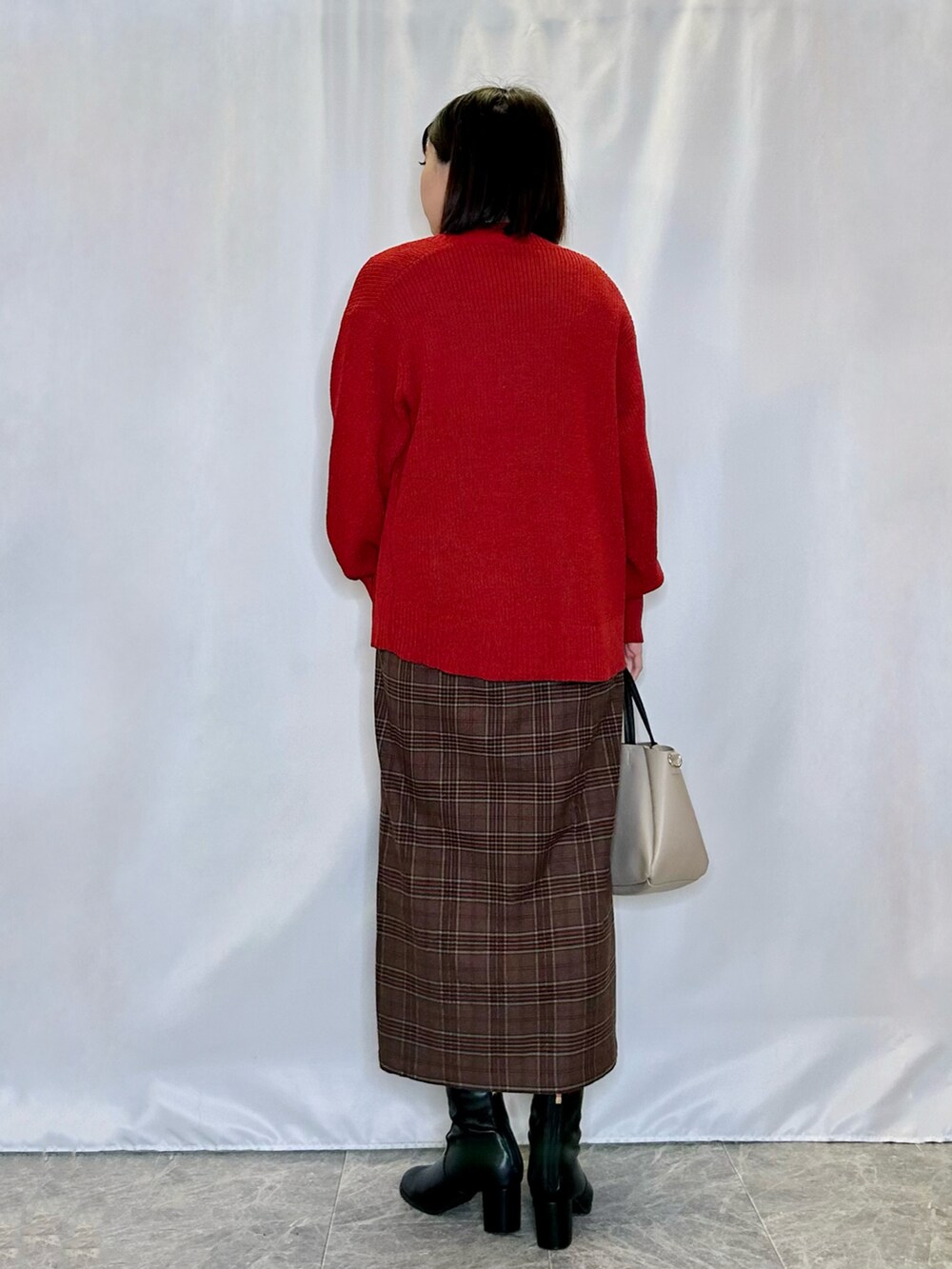 ブラック系のブーツ、ベージュ系のトートバッグ、レッド系のスカートを着用したレディースの冬コーディネートの3枚目の写真