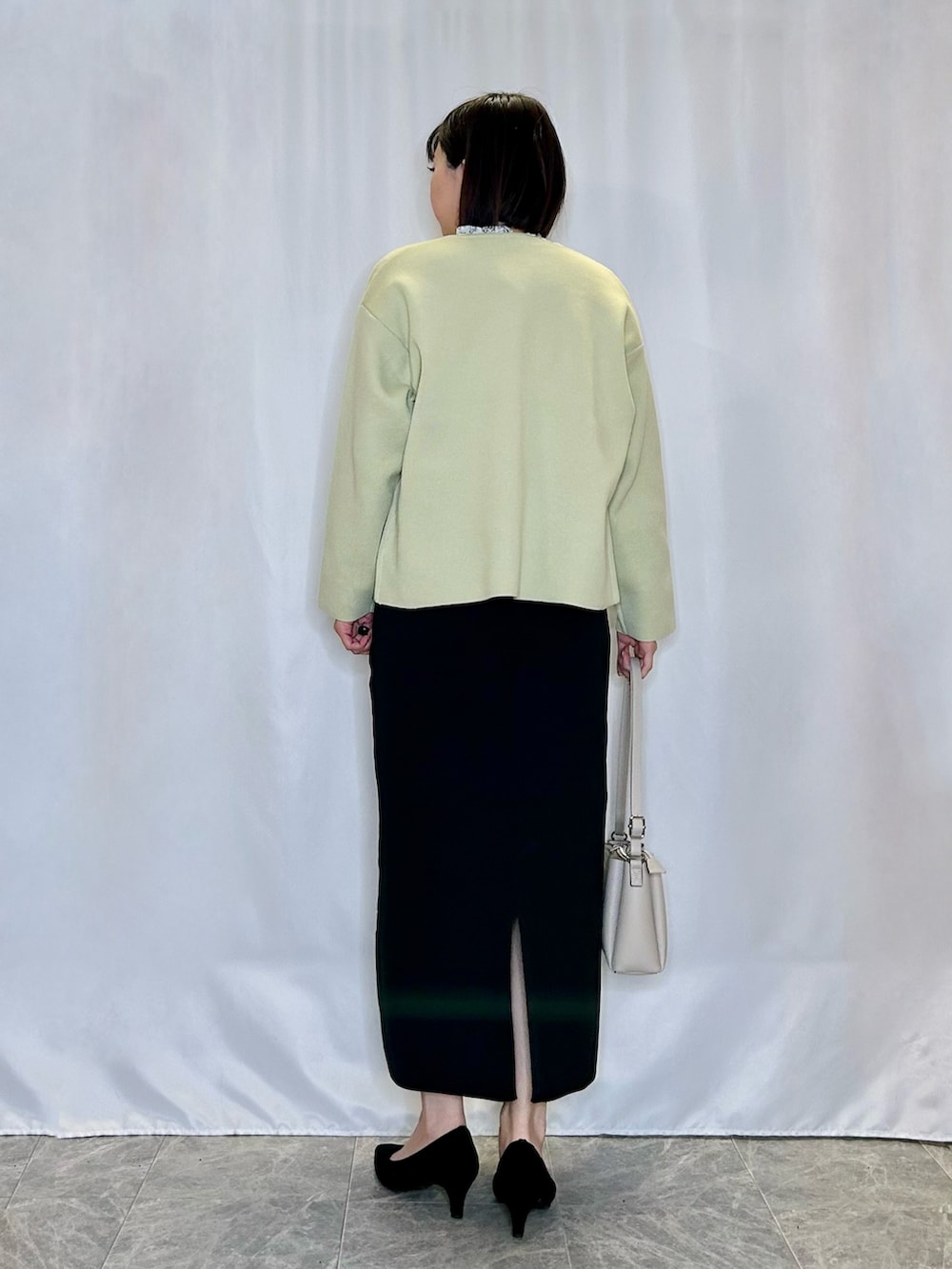 ブラック系のパンプス、ブラック系のスカート、ベージュ系のショルダーバッグを着用したレディースの春コーディネートの3枚目の写真