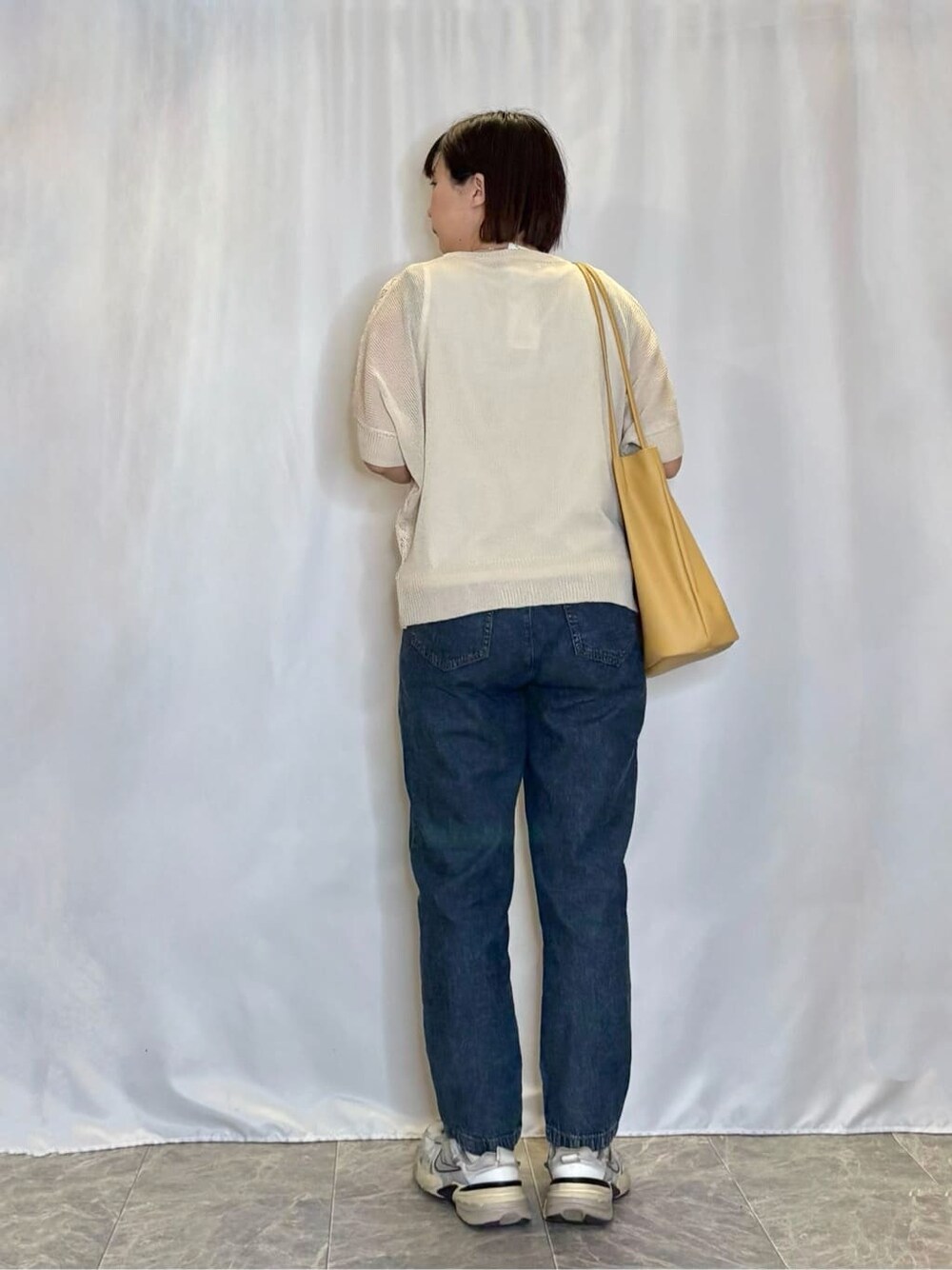ブルー系のデニムパンツ、イエロー系のトートバッグ、シルバー系のネックレスを着用したレディースの春コーディネートの3枚目の写真
