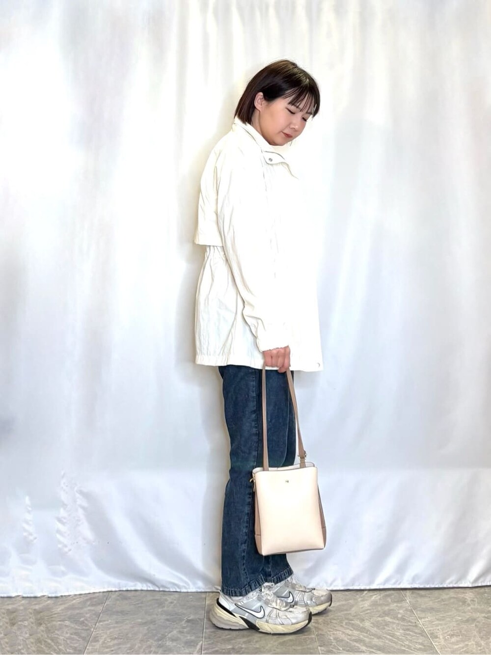 ホワイト系のブルゾン、オレンジ系のニット/セーター、ブルー系のデニムパンツを着用したレディースの春コーディネートの2枚目の写真