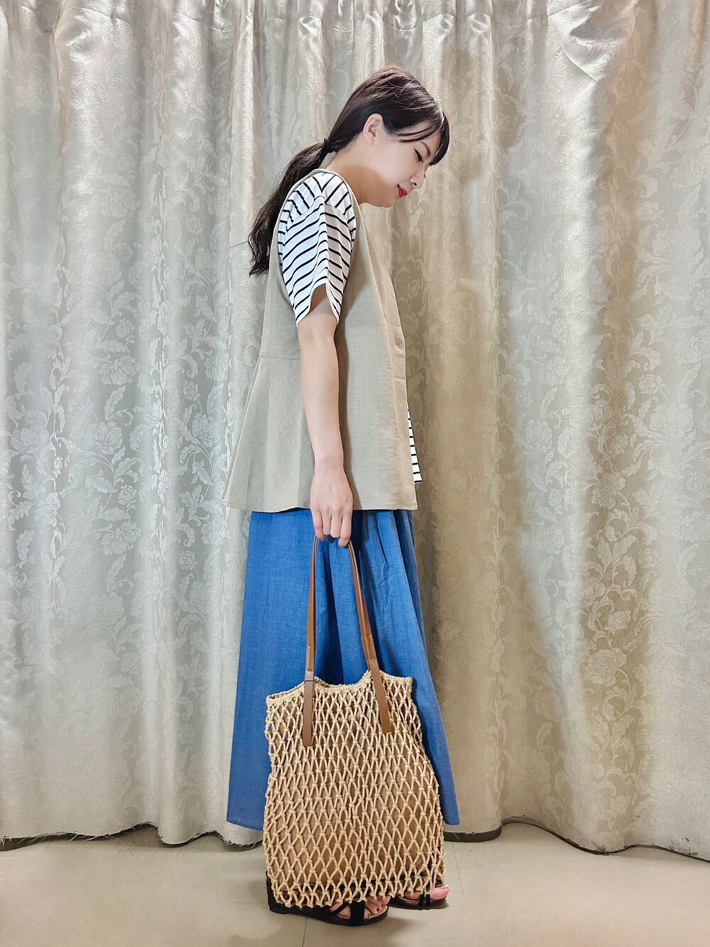 ブラウン系のトートバッグ、ブラック系のサンダル、ブルー系のスカートを着用したレディースの春コーディネートの2枚目の写真