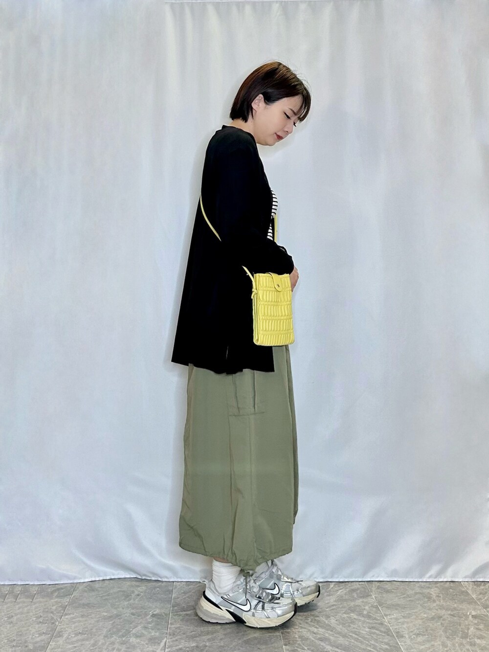 グリーン系のスカート、イエロー系のショルダーバッグ、ブラック系のカーディガン/ボレロを着用したレディースの春コーディネートの2枚目の写真