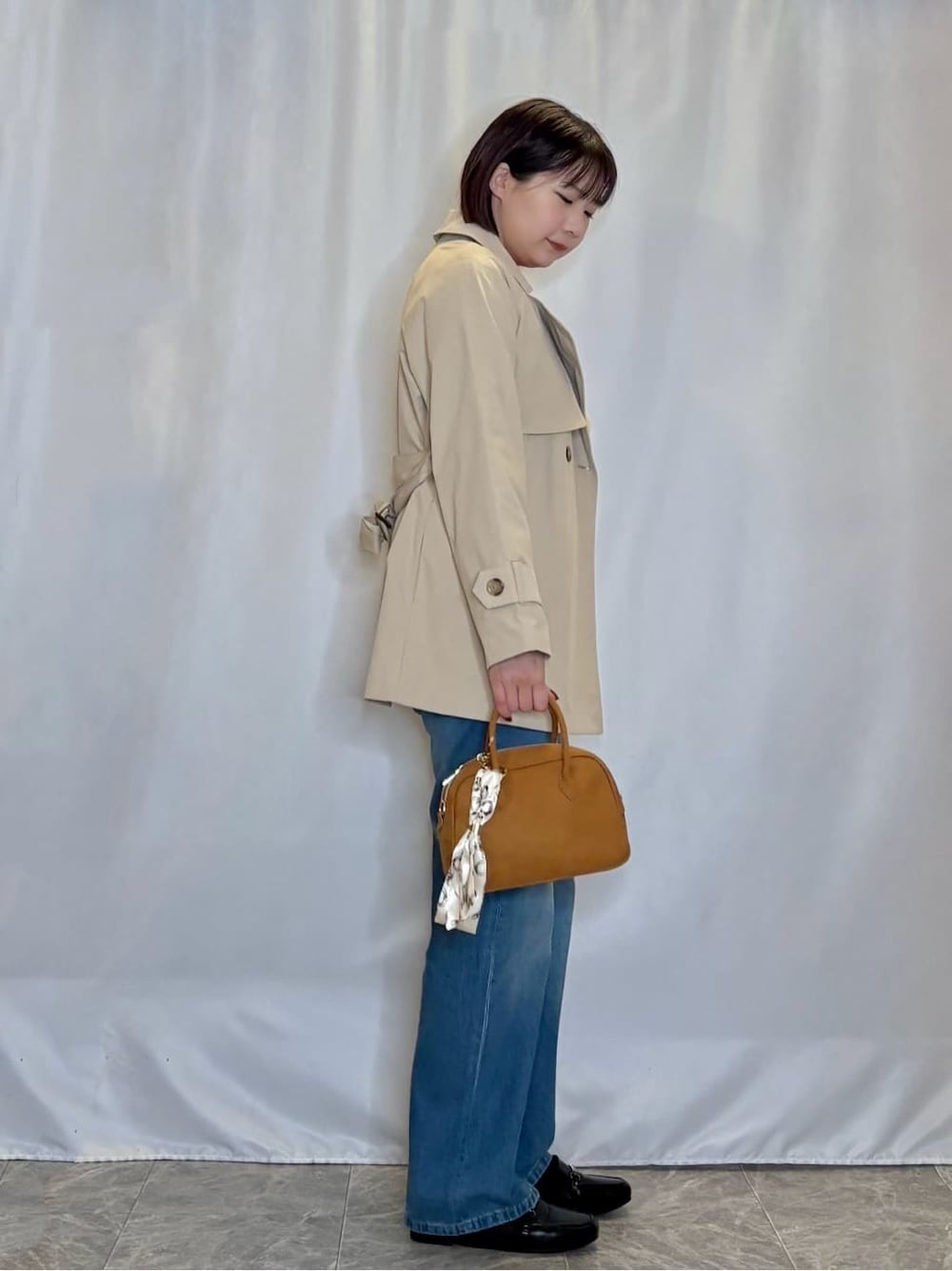 レッド系のニット/セーター、ブルー系のデニムパンツ、ベージュ系のトレンチコートを着用したレディースの冬コーディネートの2枚目の写真