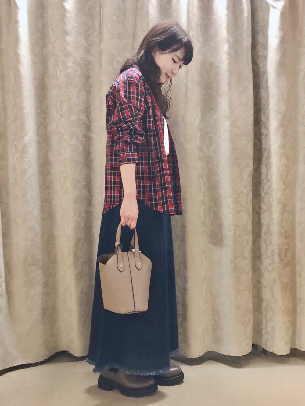 ベージュ系のトートバッグ、ブラウン系のブーツ、ブルー系のデニムスカートを着用したレディースの秋コーディネートの2枚目の写真