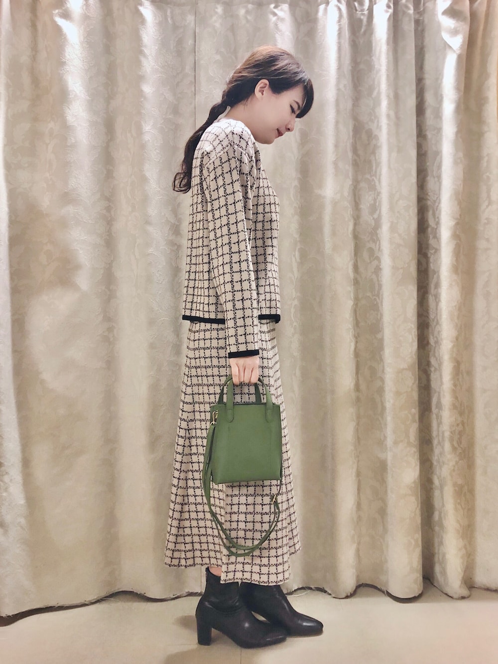 ブラック系のブーツ、グリーン系のショルダーバッグ、ベージュ系のスカートを着用したレディースの冬コーディネートの2枚目の写真