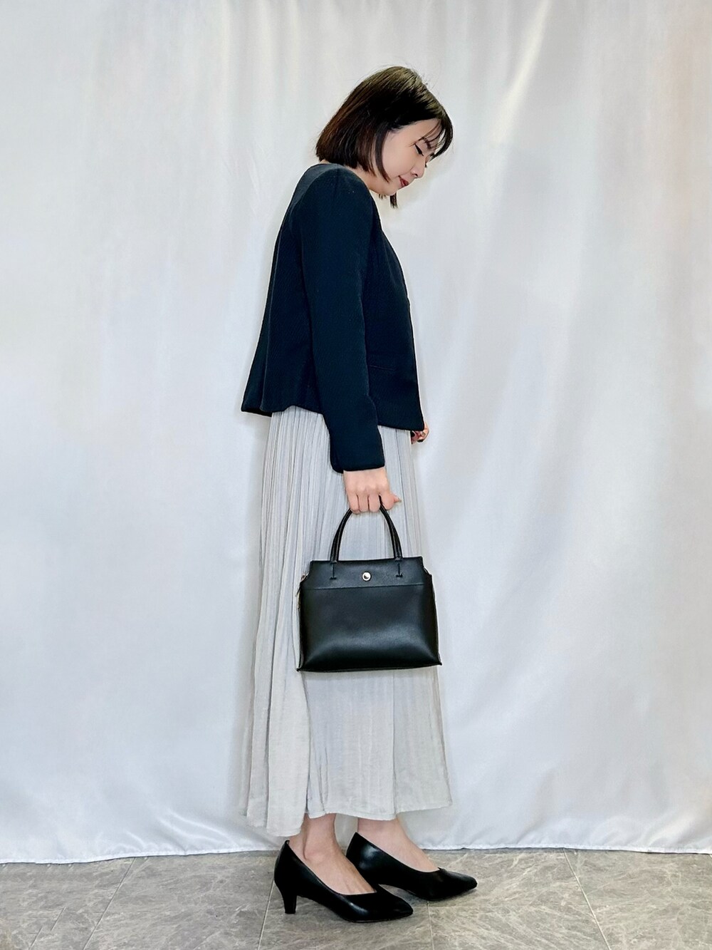 グレー系のスカート、ブラック系のパンプス、ブラック系のトートバッグを着用したレディースの冬コーディネートの2枚目の写真