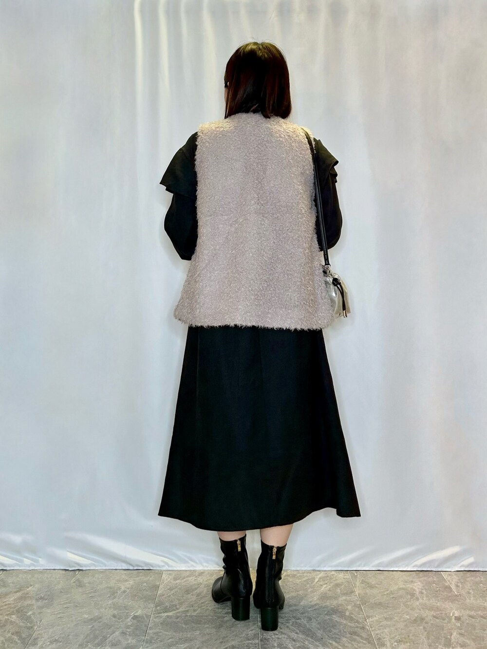 ブラック系のブーツ、シルバー系のショルダーバッグ、グレー系のベストを着用したレディースの秋コーディネートの3枚目の写真