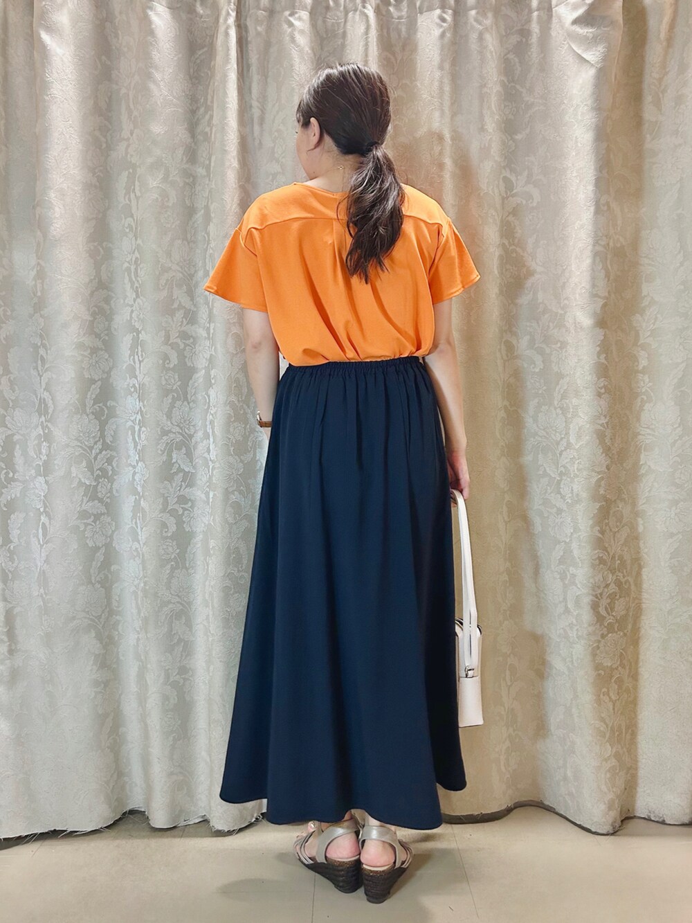 ホワイト系のショルダーバッグ、オレンジ系のTシャツ/カットソー、ゴールド系のサンダルを着用したレディースの夏コーディネートの3枚目の写真