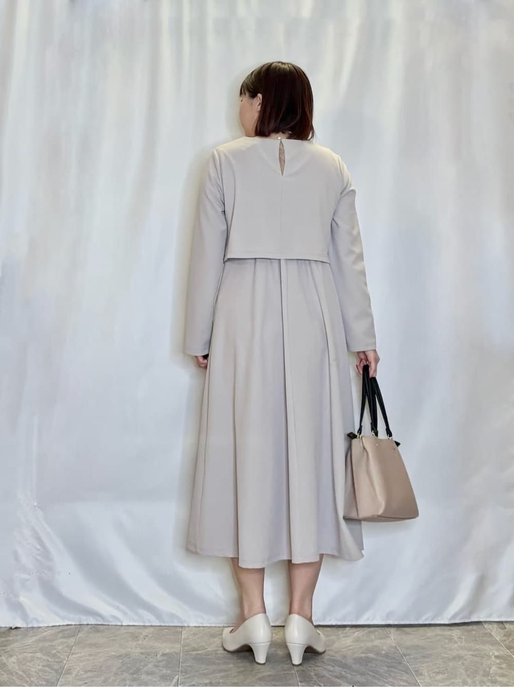 グレー系のワンピース、ホワイト系のパンプス、ベージュ系のトートバッグを着用したレディースの春コーディネートの3枚目の写真
