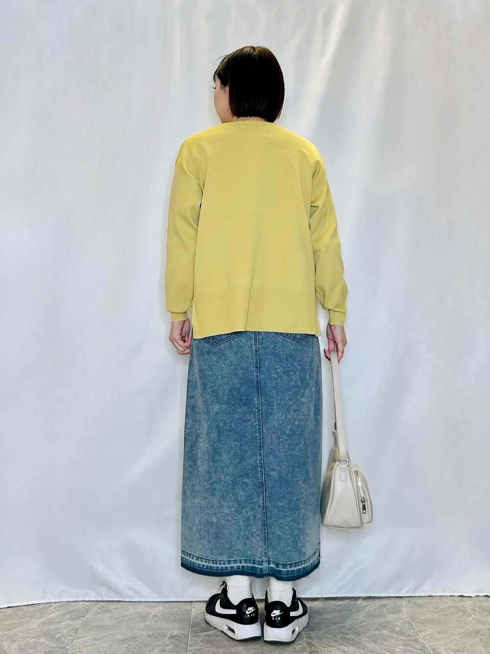 ブルー系のデニムスカート、グレー系のショルダーバッグ、イエロー系のニット/セーターを着用したレディースの冬コーディネートの3枚目の写真