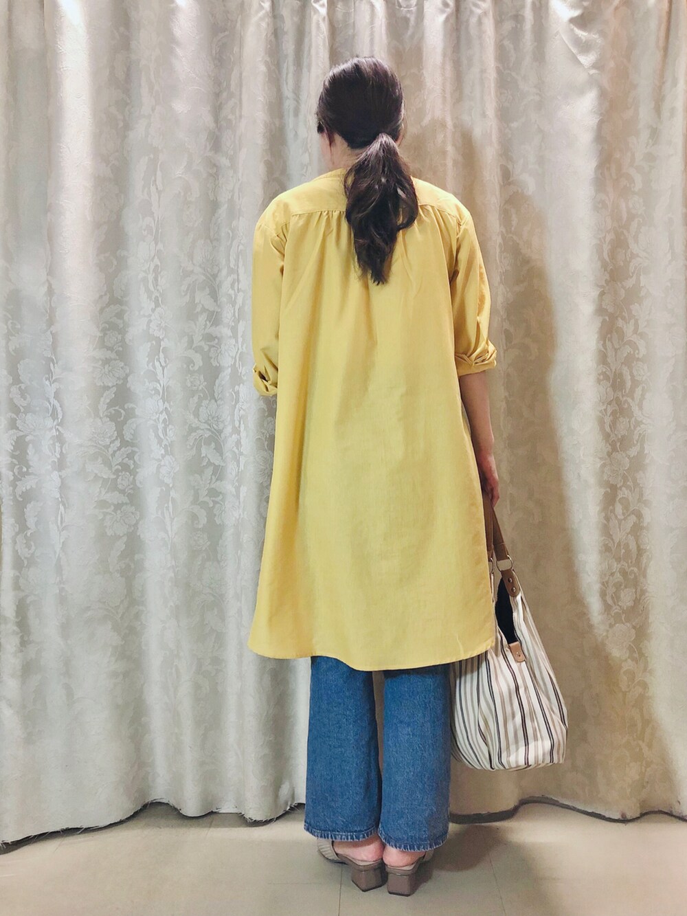 イエロー系のワンピース、ブルー系のデニムパンツ、ベージュ系のサンダルを着用したレディースの夏コーディネートの3枚目の写真