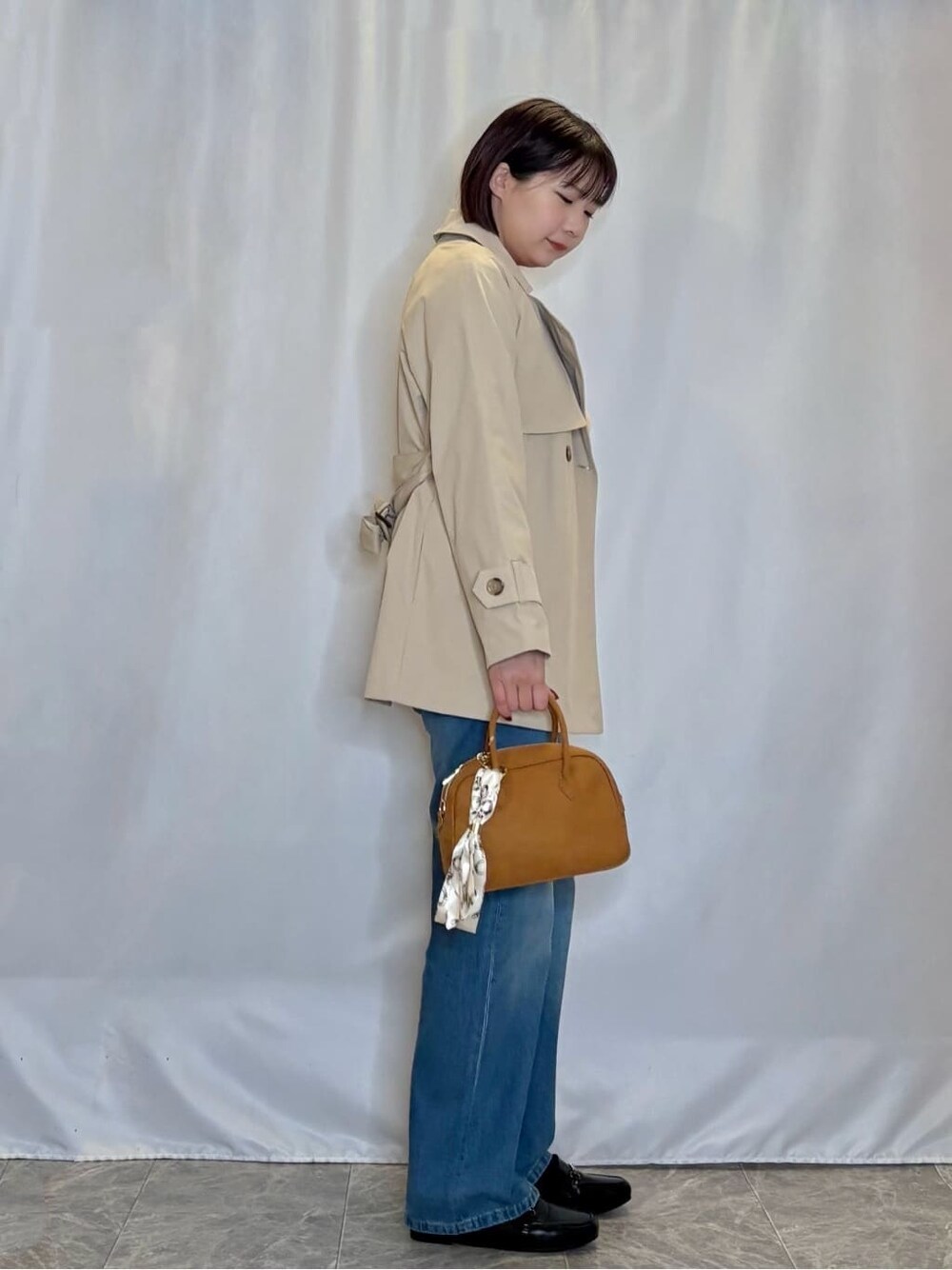 ベージュ系のトレンチコート、レッド系のニット/セーター、ブルー系のデニムパンツを着用したレディースの冬コーディネートの2枚目の写真