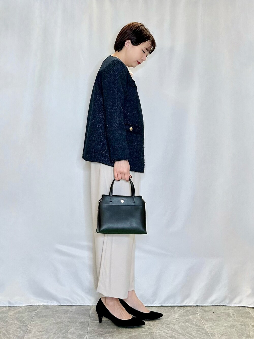 ブラック系のトートバッグ、ブラック系のパンプス、ブルー系のノーカラージャケットを着用したレディースの春コーディネートの2枚目の写真