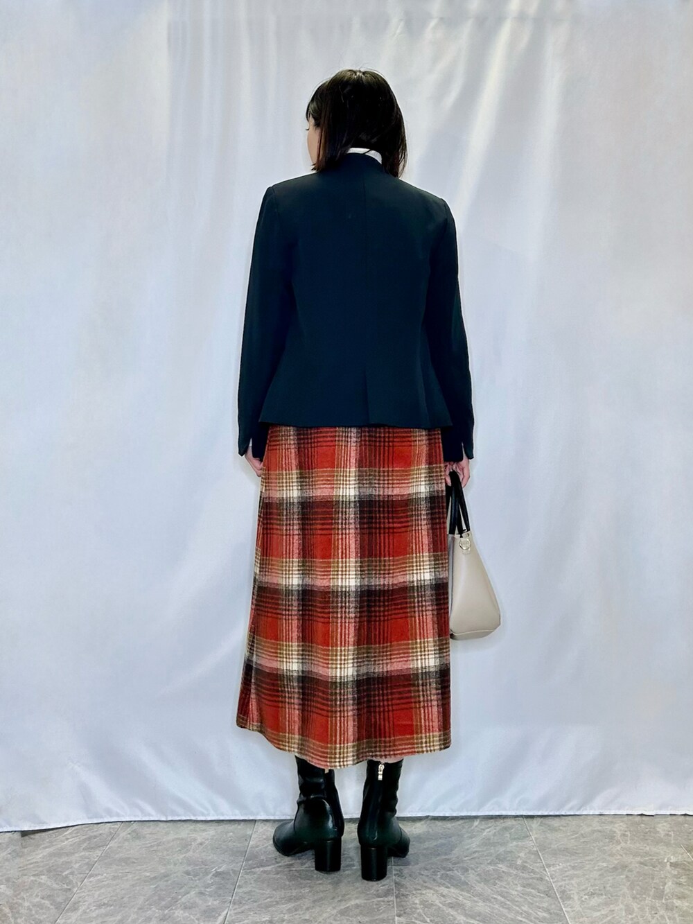 ブラック系のブーツ、レッド系のスカート、ベージュ系のトートバッグを着用したレディースの冬コーディネートの3枚目の写真