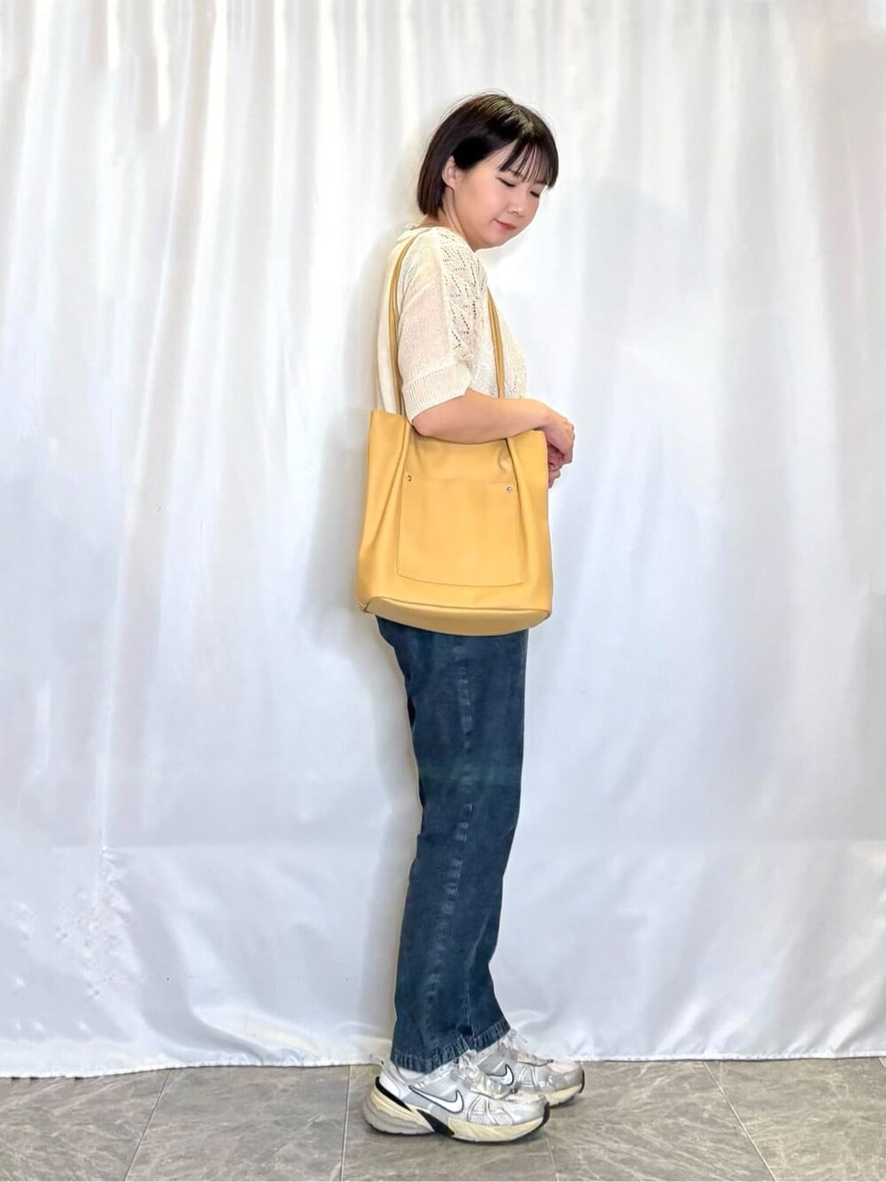 ブルー系のデニムパンツ、イエロー系のトートバッグ、シルバー系のネックレスを着用したレディースの春コーディネートの2枚目の写真