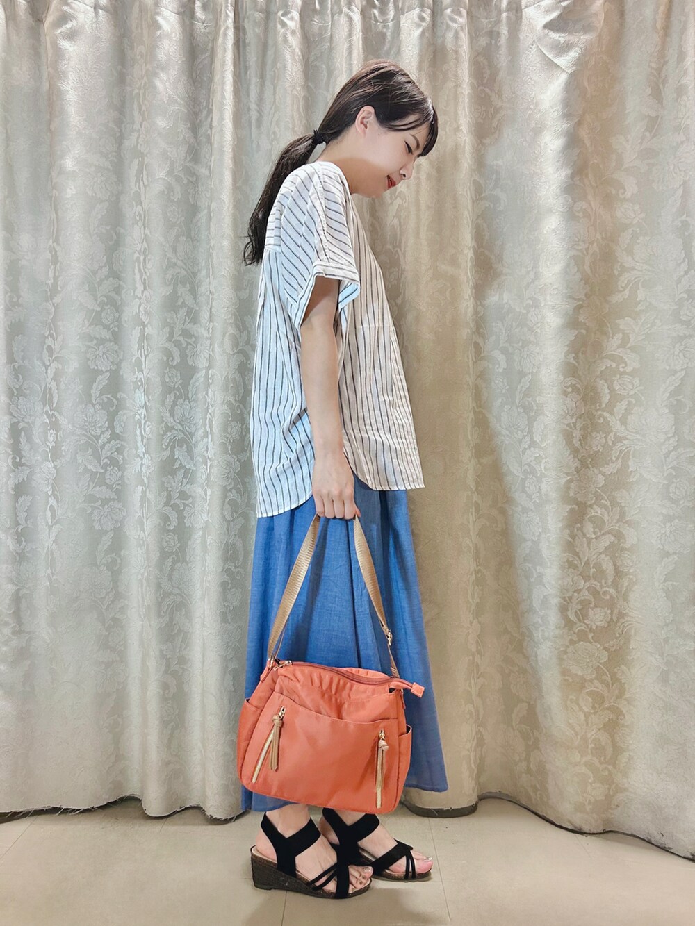 ブルー系のスカート、オレンジ系のショルダーバッグ、ブラック系のサンダルを着用したレディースの夏コーディネートの2枚目の写真