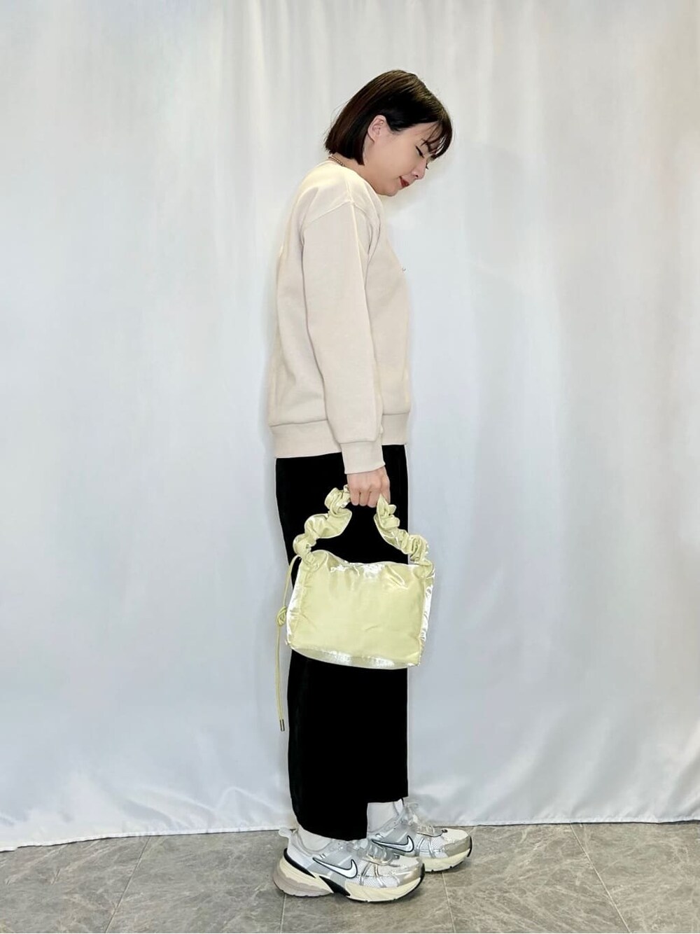 ベージュ系のTシャツ/カットソー、グレー系のスカート、イエロー系のショルダーバッグを着用したレディースの冬コーディネートの2枚目の写真