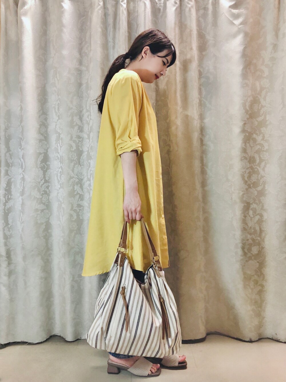 イエロー系のワンピース、ブルー系のデニムパンツ、ベージュ系のサンダルを着用したレディースの夏コーディネートの2枚目の写真