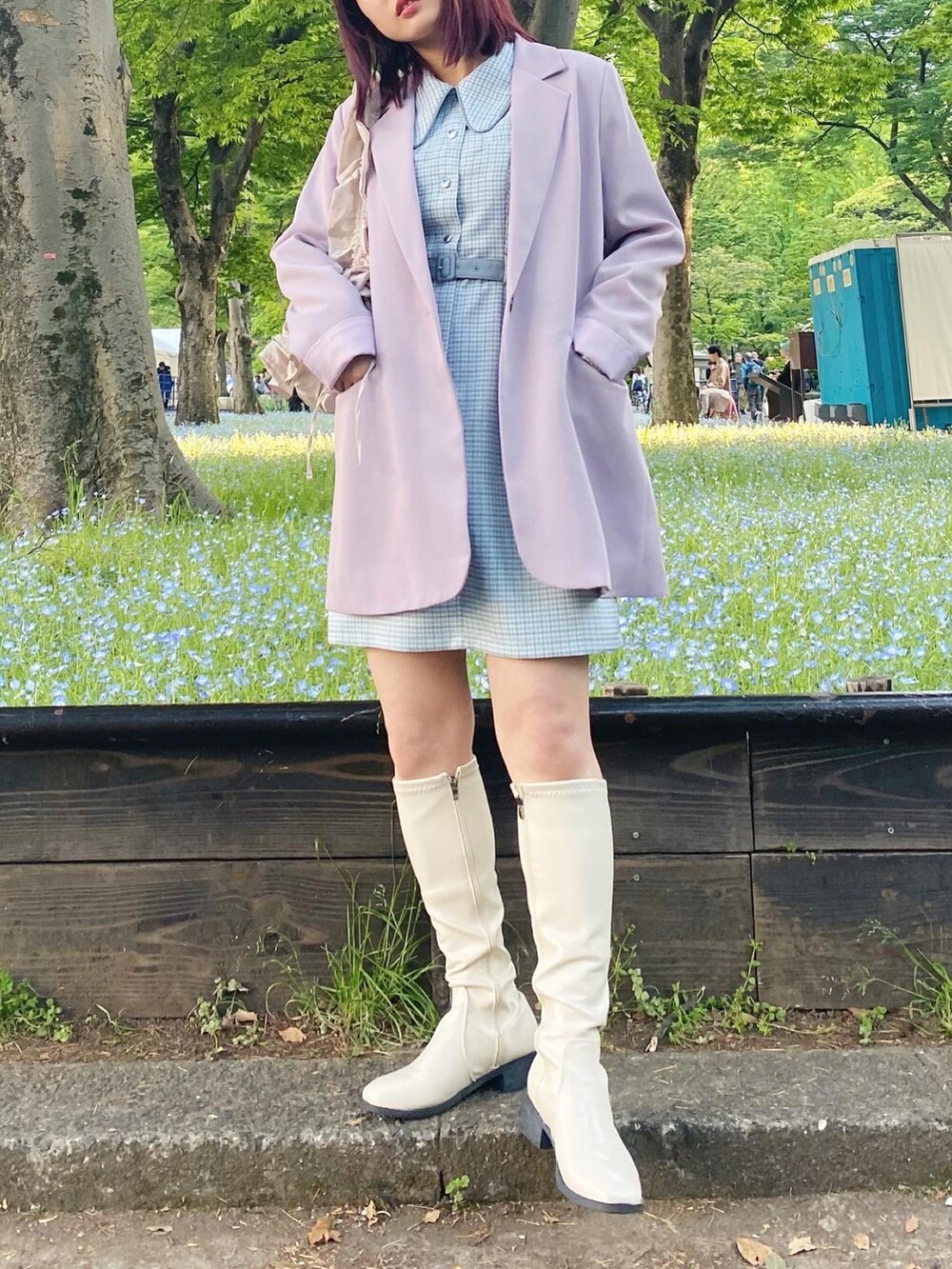 パープル系のテーラードジャケット、ホワイト系のブーツ、ブルー系のワンピースを着用したレディースの春コーディネートの2枚目の写真