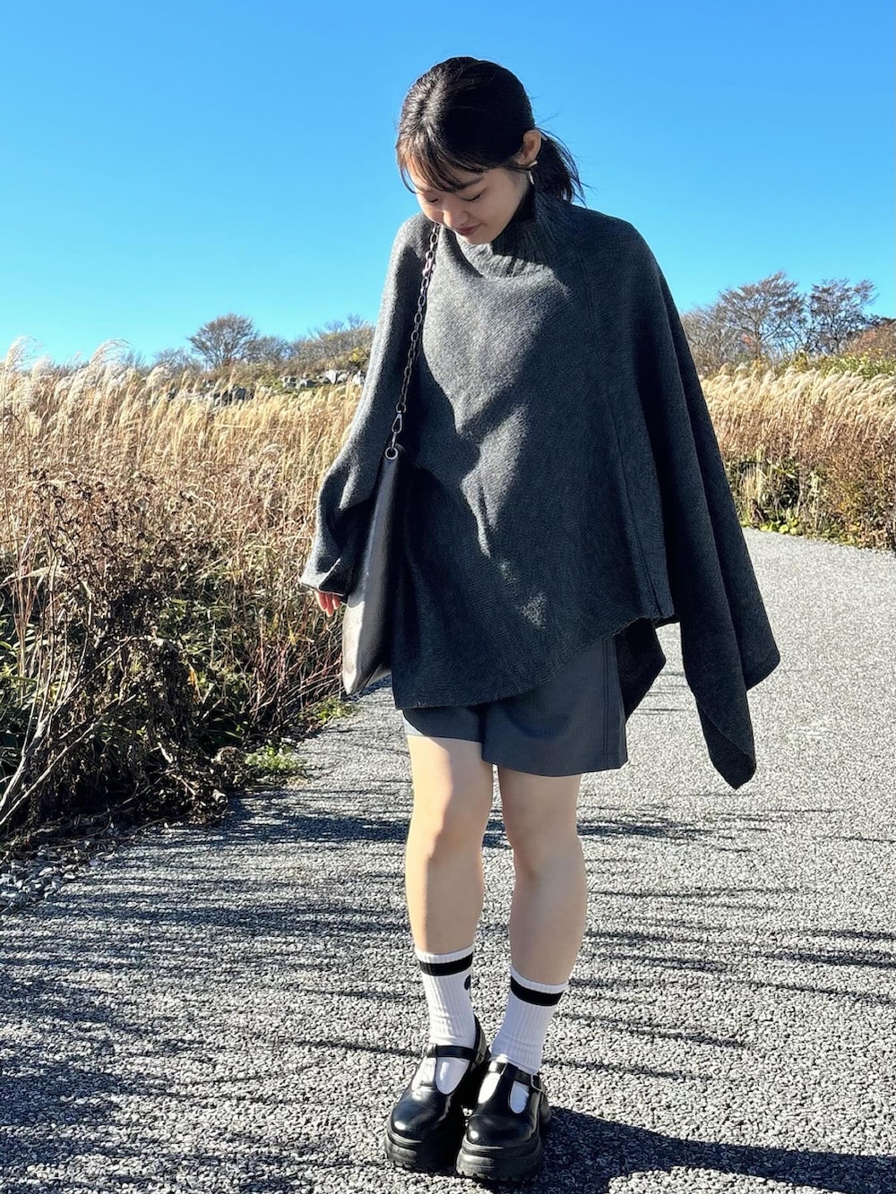 グレー系のポンチョ、グレー系のパンツ、ブラック系のローファーを着用したレディースの冬コーディネートの2枚目の写真