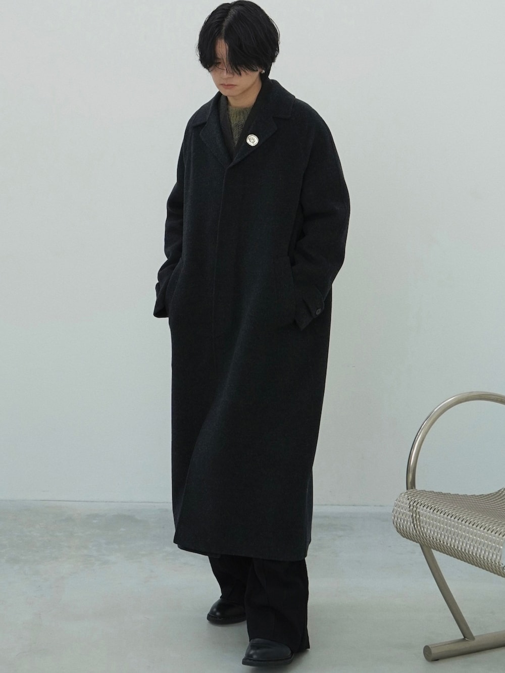 ブラック系のチェスターコート、ブラック系のテーラードジャケット、グリーン系のニット/セーターを着用したメンズの秋コーディネートの2枚目の写真