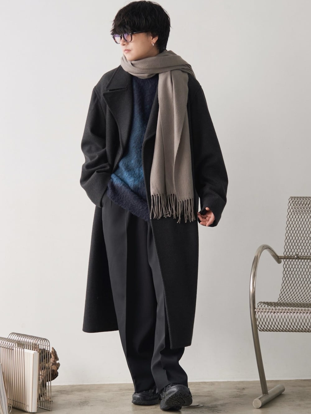 グレー系のチェスターコート、ブルー系のニット/セーター、ブラック系のスラックスを着用したメンズの冬コーディネートの2枚目の写真