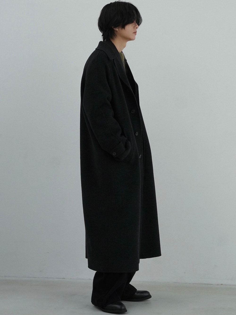 ブラック系のチェスターコート、ブラック系のテーラードジャケット、グリーン系のニット/セーターを着用したメンズの秋コーディネートの3枚目の写真